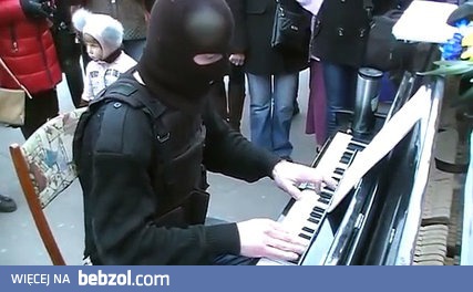 Człowiek ubrany na bojowo i w kominiarce gra na pianinie